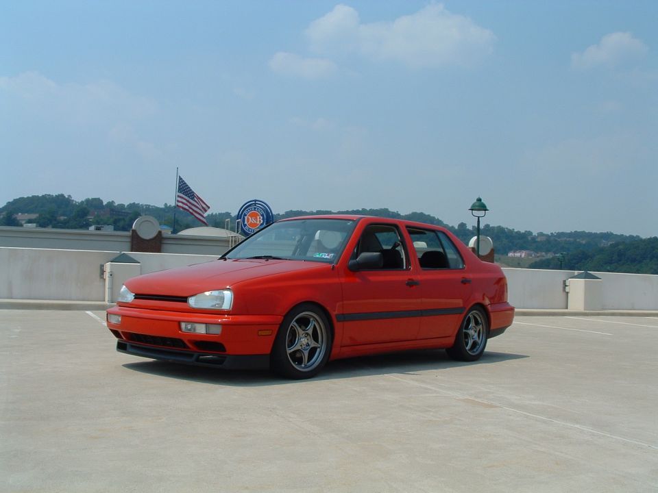 Red sedan parked on a rooftop lot, American flag and D&B sign in background