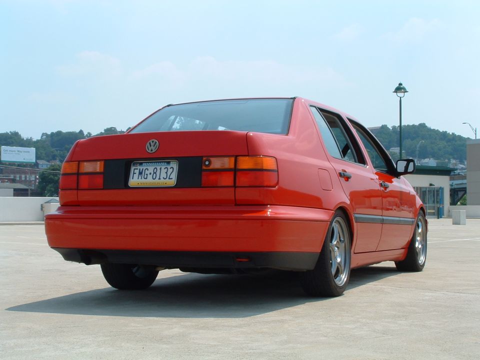 Red 1993 Volkswagen sedan, rear 3/4 view, parked on concrete. License plate FMG-8132