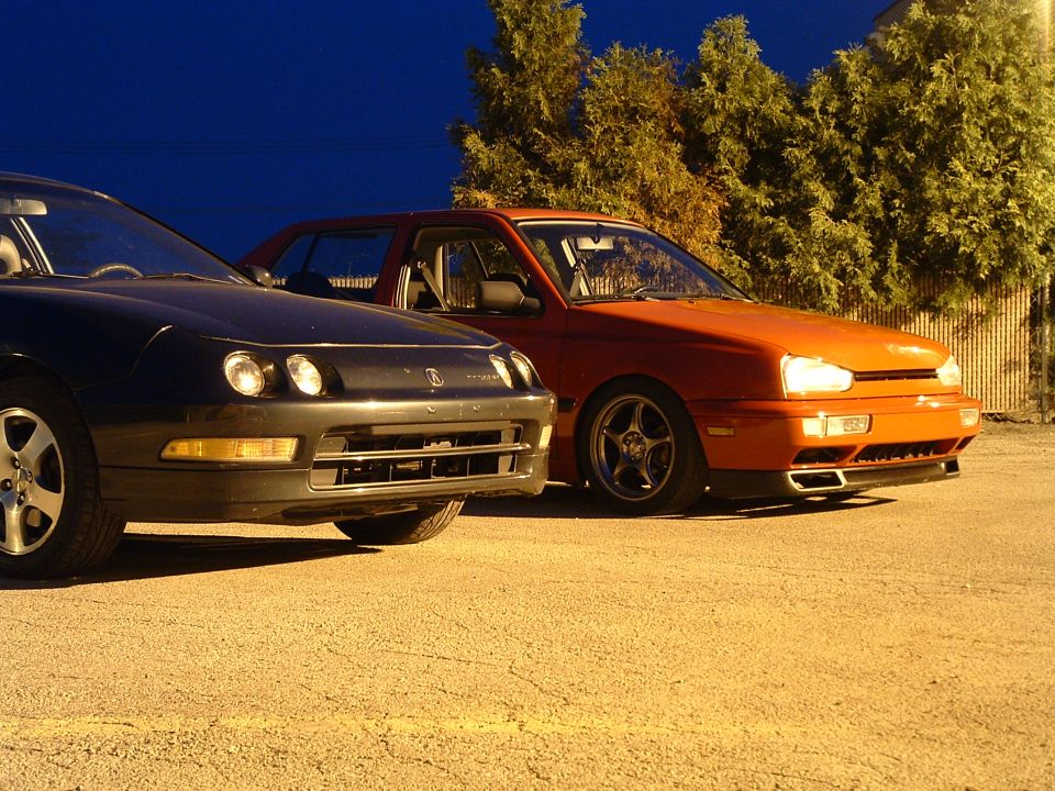 black car next to orange car, parked outside at night