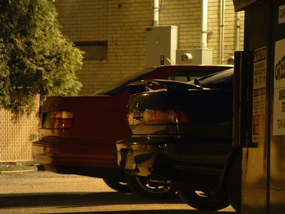 Rear view of a red car and a black car parked next to each other at night
