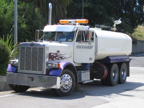 1990 Ford Bronco - white and purple Peterbilt water tanker truck with flame graphics and a roof light bar parked on a paved drive.