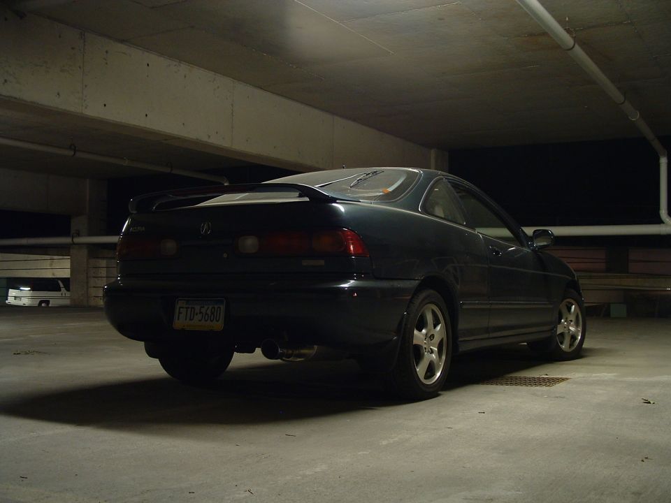 Dark coupe with a spoiler and a license plate reading FTD-5680 parked in a garage. Another white vehicle is visible in the background