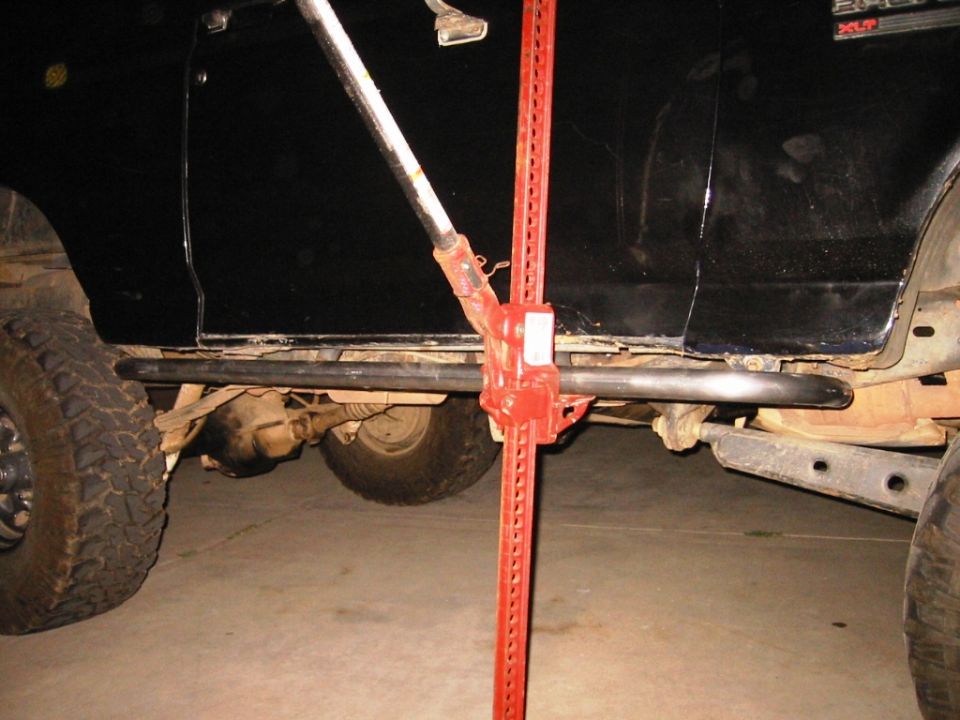 Red Hi-Lift jack under black Bronco lifting on black rock slider bar at night