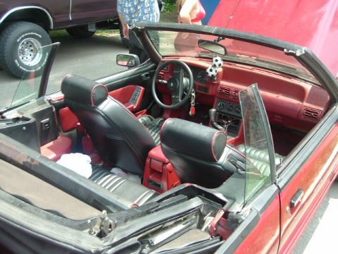 1993 Ford Taurus - The interior of a red convertible shows black seats with red trim and a red dashboard. Another vehicle is visible to the left.