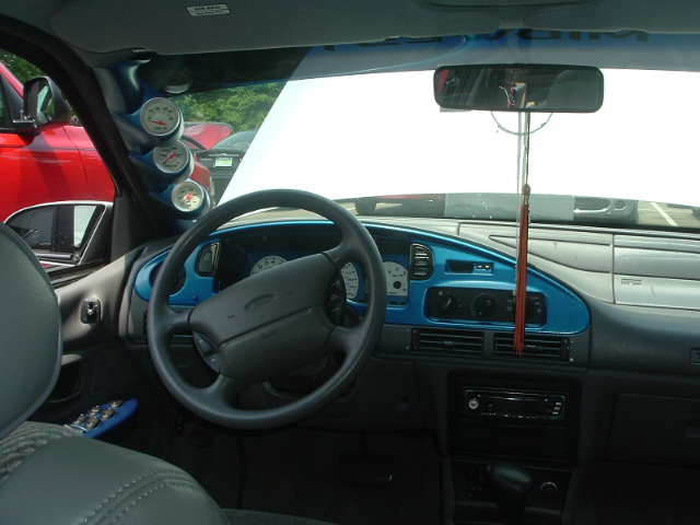 1993 Ford Taurus interior with blue dashboard trim, aftermarket gauges, and a red truck visible outside