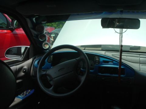 1993 Ford Taurus - The interior of a car shows aftermarket gauges and blue dashboard accents, with another vehicle visible through the window.