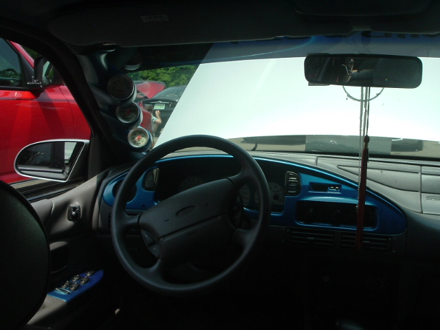 Interior view of a car with aftermarket gauges and blue trim. A red vehicle is visible outside