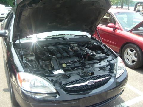 1993 Ford Taurus - Black Ford Taurus with hood open, showing engine. A red car is parked behind it.