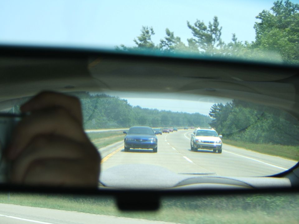 Blue sedan on highway, seen from rearview mirror