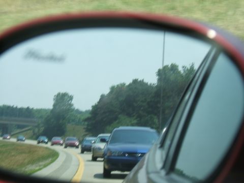 1998 Ford Taurus - View of highway traffic from a side mirror, with trees and a bridge in the background.