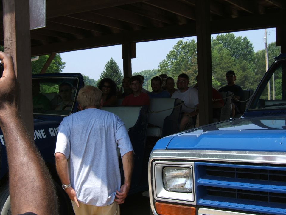 People riding in a covered wagon with a blue truck in the foreground