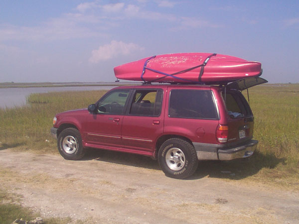 Red 1999 Ford Explorer parked on a dirt road with a kayak on its roof rack