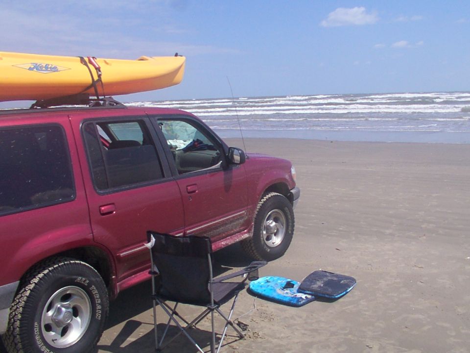 Red 1999 Ford Explorer with kayak on roof rack parked on beach