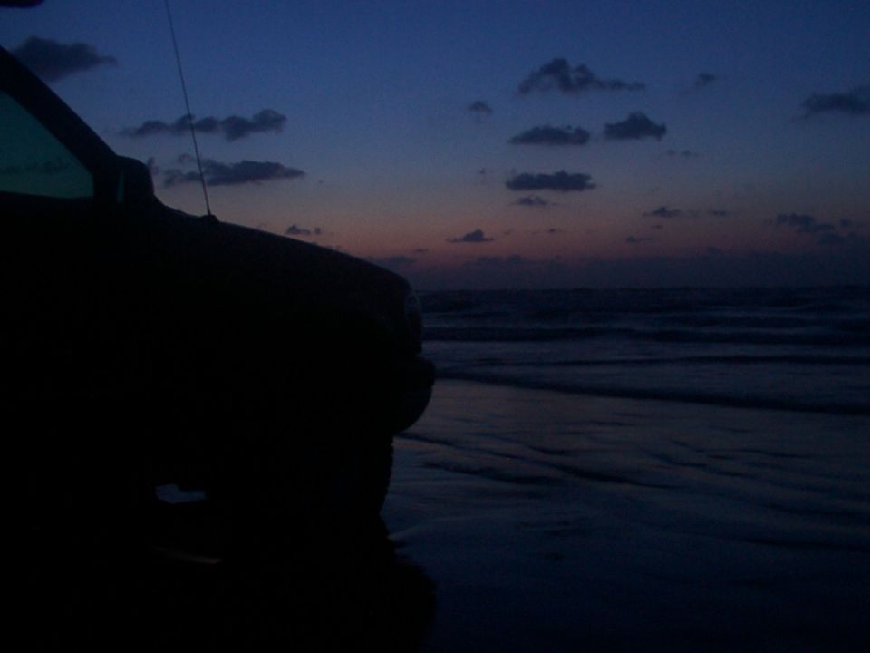 Vehicle parked on a beach with waves and clouds at dusk
