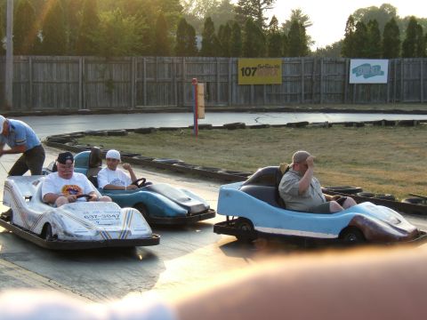 1998 Ford Taurus - Several go-karts are on a track, with drivers in each. One go-kart has visible text on its side.