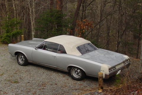 1967 Pontiac GTO - A silver 1967 Pontiac GTO convertible sits on a gravel driveway surrounded by trees.