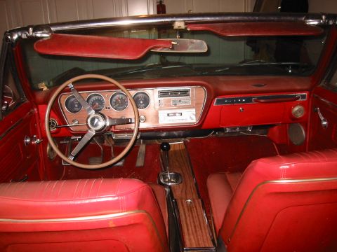 1967 Pontiac GTO - The interior of a red 1967 Pontiac GTO shows a woodgrain dashboard and classic gauges.