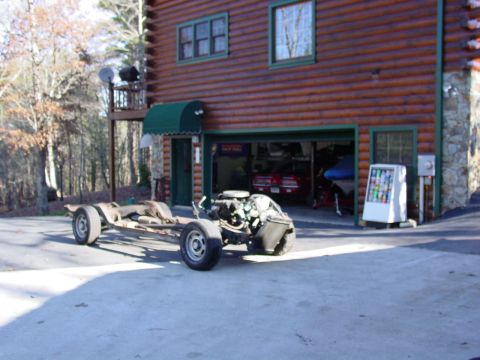 1967 Pontiac GTO - A car's chassis and engine sit outside a garage, with another vehicle visible inside.