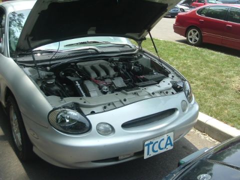 1993 Ford Taurus - Silver Ford Taurus, hood up, engine visible. License plate TCCA. Another car is parked to the right.