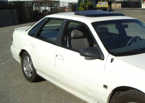 1993 Ford Taurus - This white 1993 Ford Taurus sedan is shown from a front three-quarter perspective, highlighting its sunroof and overall body style.