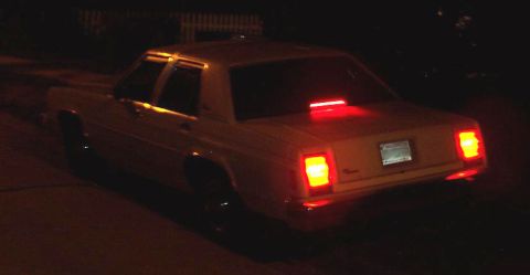 1985 Ford Crown Victoria LTD - The rear of a sedan is visible at night, with its brake lights and taillights glowing red.