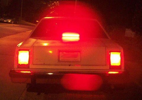 1985 Ford Crown Victoria LTD - Rear view of a white sedan at night, with bright red taillights and brake lights illuminating the scene.