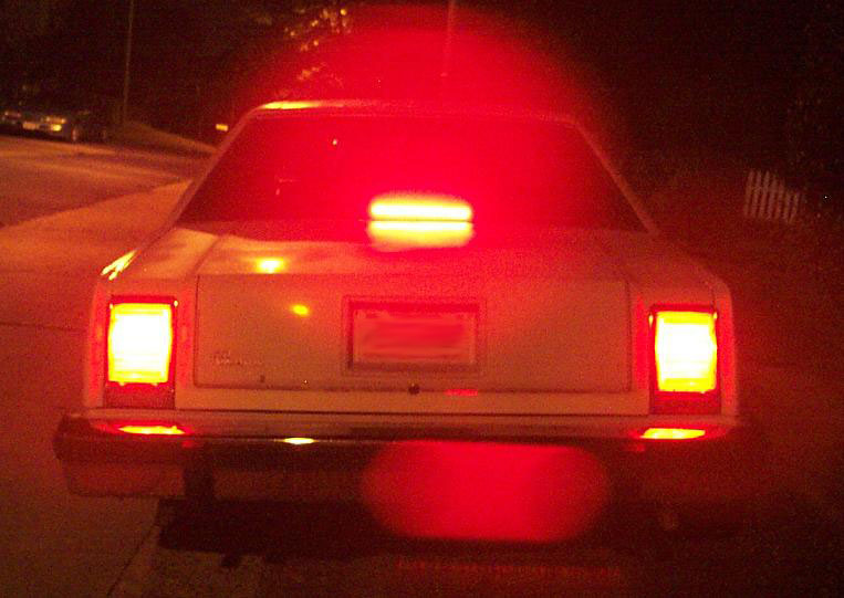 White sedan rear view at night, illuminated by red taillights and brake lights