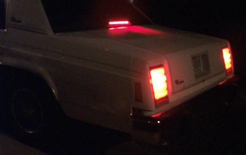 1985 Ford Crown Victoria LTD - Rear view of a white sedan at night, showing its distinctive taillights and a red light strip on the trunk.