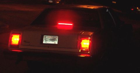 1985 Ford Crown Victoria LTD - Rear view of a 1985 Ford Crown Victoria LTD at night, showing illuminated brake lights.
