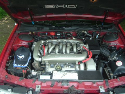 1993 Ford Taurus - The engine bay of a red 1993 Ford Taurus SHO, a V8 engine and a baseball cap on the battery.