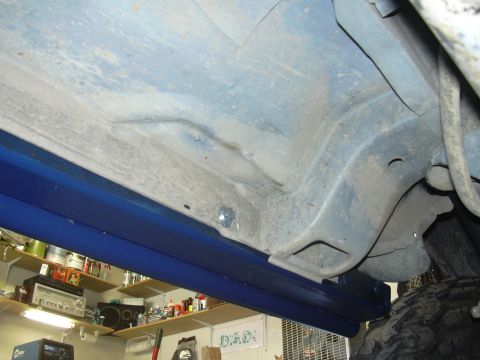 1991 Ford Bronco - Vehicle undercarriage with newly installed blue rock sliders. Garage interior visible.