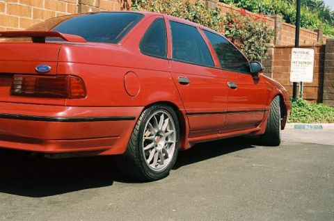 1991 Ford Taurus - This red sedan is parked next to a brick wall with a "No Parking" sign visible.