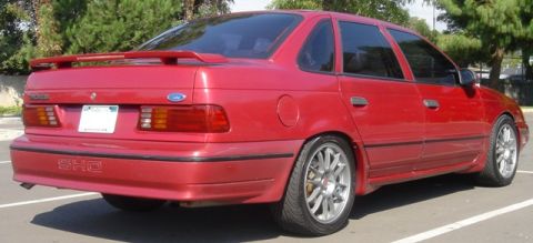 1991 Ford Taurus - Three-quarter rear view of a red Ford Taurus SHO sedan in a parking lot, with 'SHO' lettering molded into the rear bumper cover and a tall…