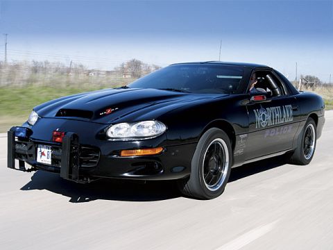 2000 Ford Crown Victoria - A black police car with a push bar is driving on a road.