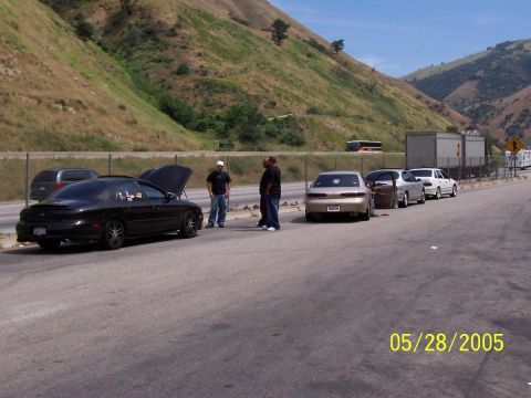 1993 Ford Taurus - Several cars are parked on the side of a highway with a grassy hill in the background.