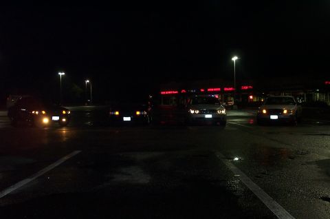 1999 Ford Crown Victoria - Night meet in a wet strip-mall parking lot with four sedans lined up facing the camera, headlights and fog lamps burning. One car in the mi…