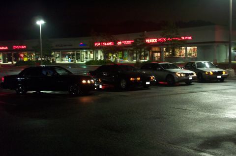 1999 Ford Crown Victoria - Nighttime parking-lot scene showing four full-size sedans lined up in front of a lit strip mall with signs for Fox Liquors, Trader and Radi…
