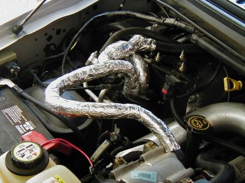 2002 Ford Excursion - Insulated pipes and hoses in an engine bay, with a battery and other engine components visible.