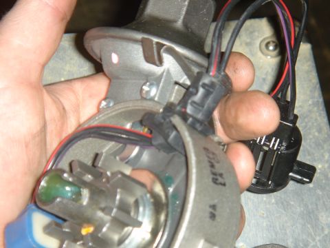 1986 Ford Mustang - Close-up of a car's distributor assembly, held by a hand, with electrical connectors and wires visible.