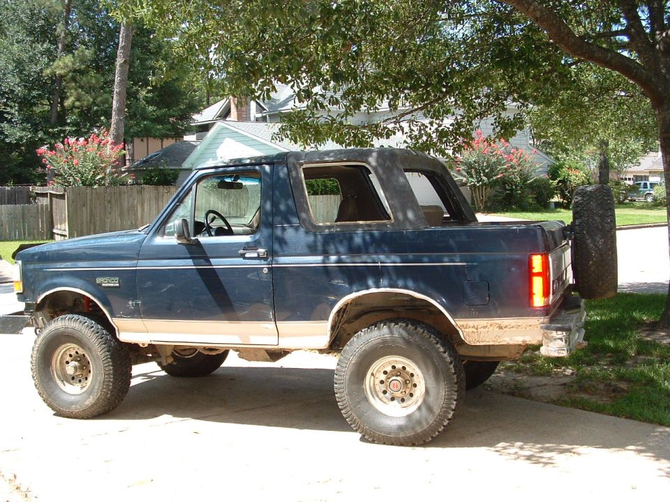 Lifted blue and tan Ford Bronco SUV on off-road tires, side view in a driveway.