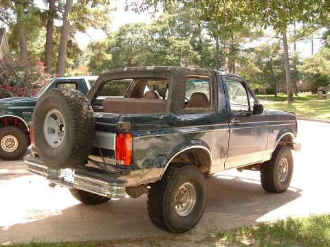 1993 Ford Bronco - Rear view of a 1993 Ford Bronco, showing its spare tire and the side of another vehicle.