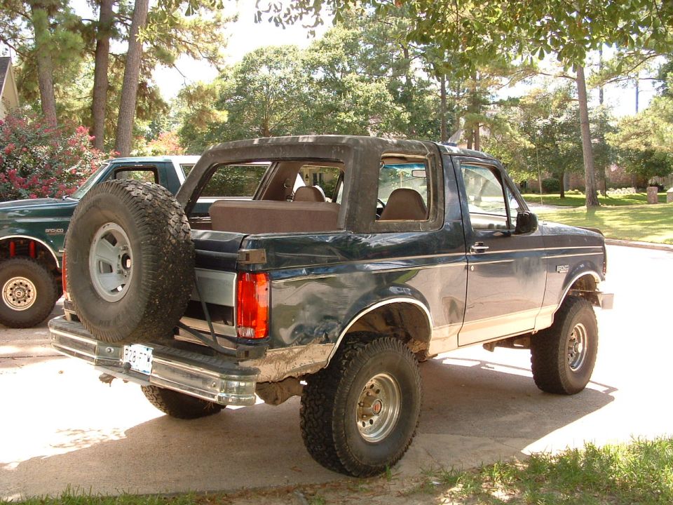 Teal Ford Bronco with rear spare tire and lift kit, rear 3/4 view in driveway