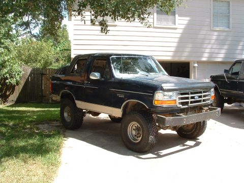1993 Ford Bronco - This lifted Ford Bronco is parked in a driveway next to another truck, with a house in the background.