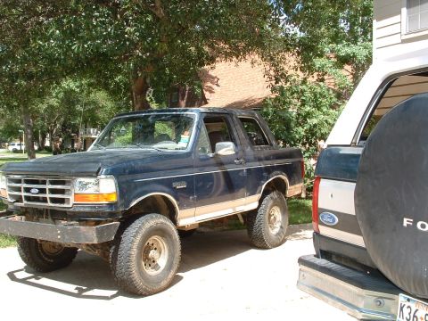 1993 Ford Bronco - A dark blue Ford Bronco is parked next to another vehicle, showing its front 3/4 view.