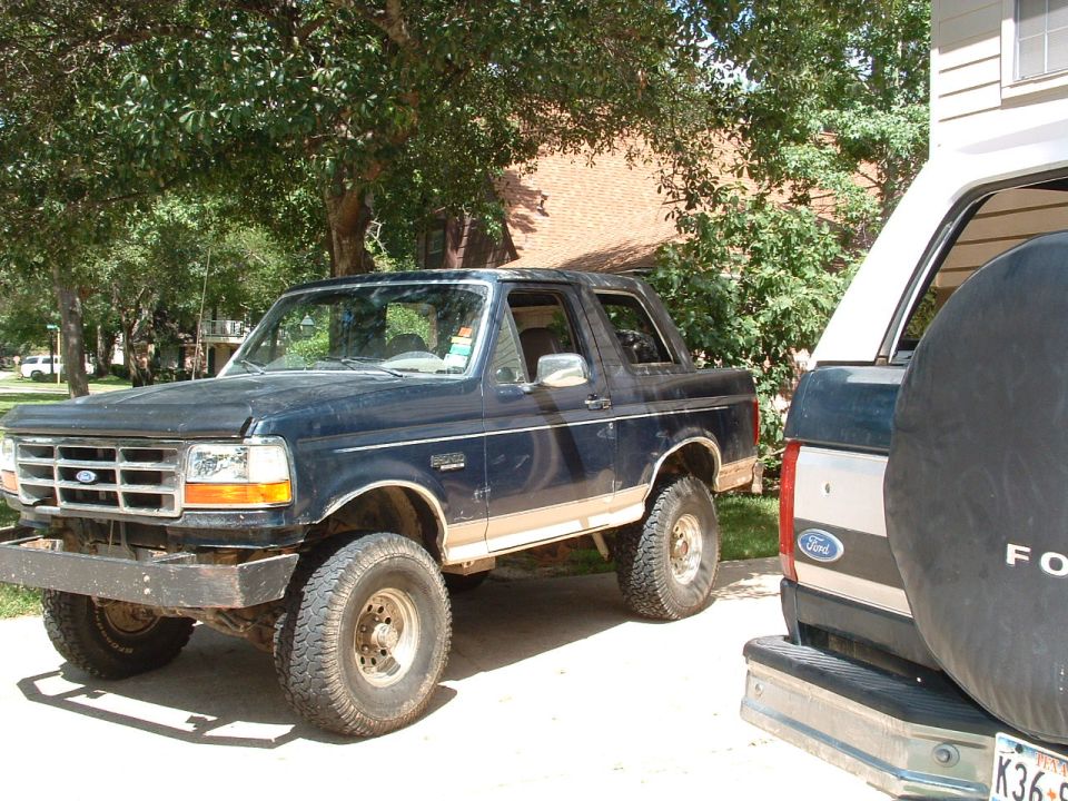 Dark blue Ford Bronco with tan lower trim, lifted suspension, and aftermarket bumper