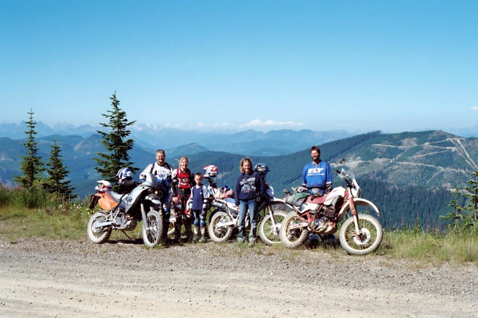 Riders and three dual-sport motorcycles parked on gravel mountain road overlook