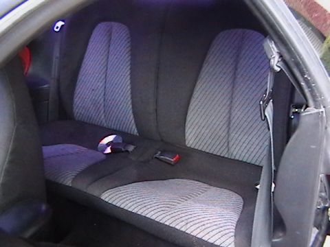 1993 Ford Probe - The rear interior of a car shows patterned seats and seatbelts, with a CD resting on the seat.