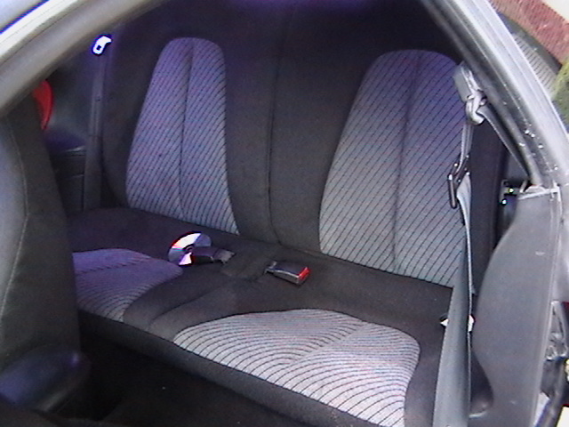 Car interior rear seats with patterned fabric and seatbelts. A CD is on the seat