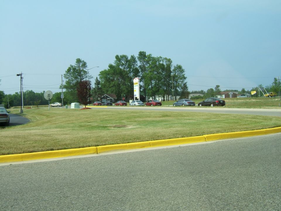 Several cars parked and driving on a road with a grassy median and trees