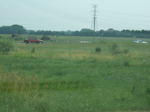 1998 Ford Taurus - Two sedans are seen driving through a wide, grassy field under a hazy sky with a large power line tower in the background.